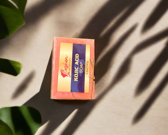 Kojic Acid Soap packaging against a neutral background with shadows and green leaves.