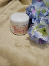 Turmeric Ascorbic Acid Cream jar next to blue and purple flowers on a soft surface.